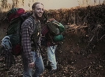 Movie still from “The Blair Witch Project” (1999), directed by Eduardo Sánchez – A man with a beard is walking in the woods with a backpack; Medium shot, High angle