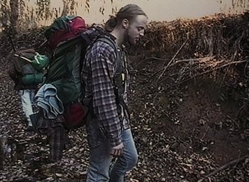 Movie still from “The Blair Witch Project” (1999), directed by Eduardo Sánchez – A man walking with a large backpack on his back; Wide shot, High angle