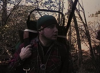 Movie still from “The Blair Witch Project” (1999), directed by Eduardo Sánchez – A man with a backpack walking through the woods; Medium shot, Low angle