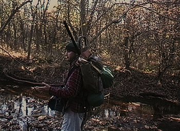 Movie still from “The Blair Witch Project” (1999), directed by Eduardo Sánchez – A man walking through the woods with a backpack on his back; Wide shot, High angle