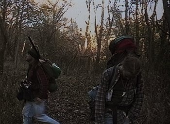 Movie still from “The Blair Witch Project” (1999), directed by Eduardo Sánchez – Two people walking through the woods with backpacks on; Wide shot, High angle