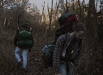 Movie still from “The Blair Witch Project” (1999), directed by Eduardo Sánchez – Two people walking through the woods wearing backpacks; Wide shot, High angle