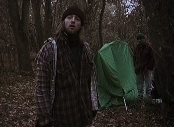 Movie still from “The Blair Witch Project” (1999), directed by Eduardo Sánchez – A man standing next to a tent in the woods; Medium shot, Low angle