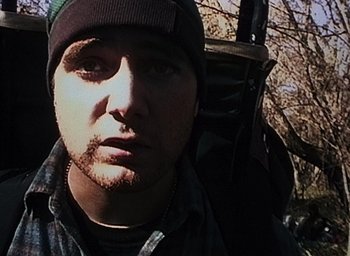 Movie still from “The Blair Witch Project” (1999), directed by Eduardo Sánchez – A person wearing a hat with trees in the background; Close Up shot, High angle