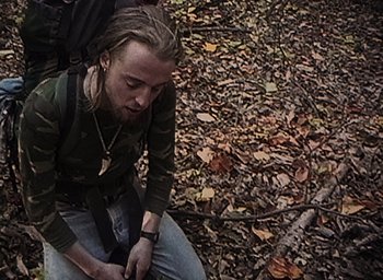 Movie still from “The Blair Witch Project” (1999), directed by Eduardo Sánchez – A man sitting on the ground in the woods; Medium shot, Overhead angle