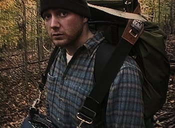 Movie still from “The Blair Witch Project” (1999), directed by Eduardo Sánchez – A man in a plaid shirt with a large backpack on his back; Medium shot, High angle