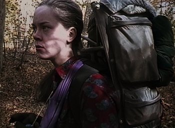 Movie still from “The Blair Witch Project” (1999), directed by Eduardo Sánchez – A woman with a large backpack walking through the woods; Close Up shot, Low angle