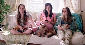 Three young women sitting on a couch next to a dog