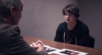 Movie still from “The Bling Ring” (2013), directed by Sofia Coppola – A man sitting at a table with a picture of a woman; Medium shot, Over the shoulder angle