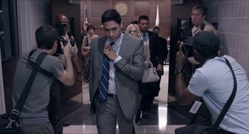 Movie still from “The Bling Ring” (2013), directed by Sofia Coppola – A man in a gray suit and a blue tie standing in a hallway; Medium shot, Over the shoulder angle