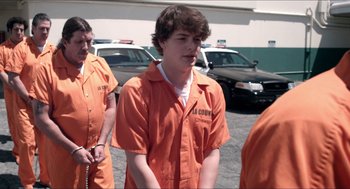 Movie still from “The Bling Ring” (2013), directed by Sofia Coppola – A group of men in orange jumpsuits standing next to each other in a parking lot; Medium shot, Over the shoulder angle