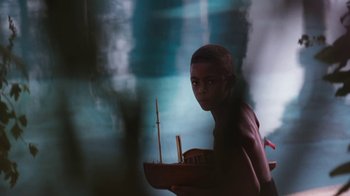 Movie still from “The Bodyguard” (1992), directed by Mick Jackson – A young man holding a small boat in front of a mirror; Medium shot, High angle