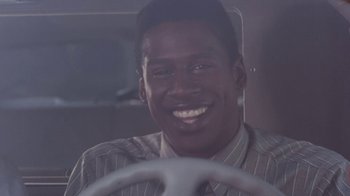 Movie still from “The Bodyguard” (1992), directed by Mick Jackson – A man smiles while sitting in a car; Close Up shot, Low angle