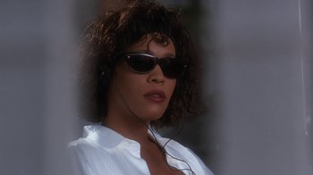 Movie still from “The Bodyguard” (1992), directed by Mick Jackson – A person wearing sunglasses and a white shirt; Close Up shot, Low angle