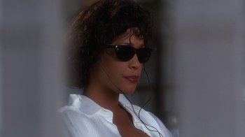 Movie still from “The Bodyguard” (1992), directed by Mick Jackson – A woman wearing sunglasses and a white shirt; Close Up shot, Low angle
