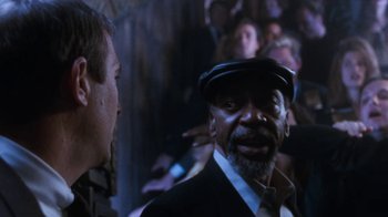 Movie still from “The Bodyguard” (1992), directed by Mick Jackson – A man with a beard and a hat talking to another man in a crowd of onlookers; Close Up shot, Over the shoulder angle