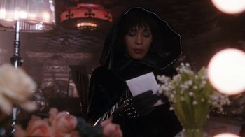 Movie still from “The Bodyguard” (1992), directed by Mick Jackson – A woman in a black outfit holding an envelope in her hands; Medium shot, Over the shoulder angle