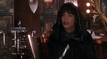 Movie still from “The Bodyguard” (1992), directed by Mick Jackson – A woman sitting at a dining table wearing a hood; Close Up shot, Over the shoulder angle