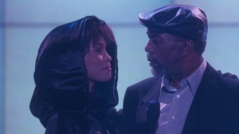 Movie still from “The Bodyguard” (1992), directed by Mick Jackson – A man and a woman standing next to each other in front of a microphone; Close Up shot, High angle