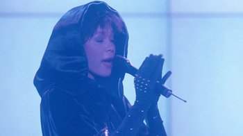 Movie still from “The Bodyguard” (1992), directed by Mick Jackson – A woman in a black outfit holding a microphone and wearing gloves; Close Up shot, High angle