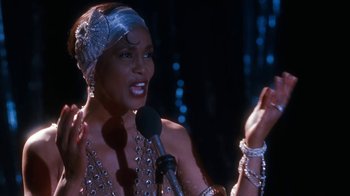 Movie still from “The Bodyguard” (1992), directed by Mick Jackson – A woman is speaking into a microphone in front of lights; Close Up shot, Over the shoulder angle