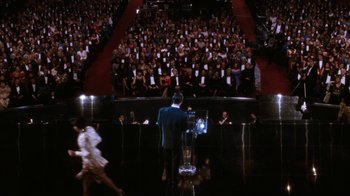 Movie still from “The Bodyguard” (1992), directed by Mick Jackson – A crowd of people in an auditorium with a man in a black suit; Extreme Wide shot, High angle