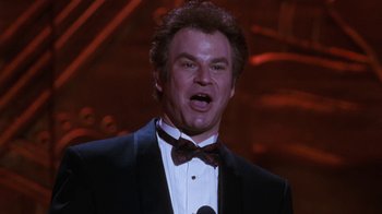 Movie still from “The Bodyguard” (1992), directed by Mick Jackson – A man wearing a suit and a bow tie while holding a microphone in front of him; Close Up shot, Low angle