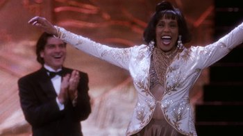 Movie still from “The Bodyguard” (1992), directed by Mick Jackson – A woman in a white and gold jacket and a man in a black suit; Medium shot, Low angle