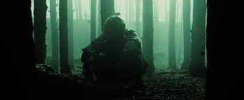 Movie still from “The Book of Eli” (2010), directed by Allen Hughes – A person in a hooded jacket crouching in the woods; Wide shot, Low angle