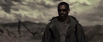 Movie still from “The Book of Eli” (2010), directed by Allen Hughes – A man in a jacket and sunglasses standing in front of a cloudy sky; Medium shot, Low angle