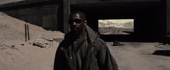 Movie still from “The Book of Eli” (2010), directed by Allen Hughes – A man wearing sunglasses and a jacket in front of a screen; Wide shot, High angle