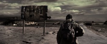 Movie still from “The Book of Eli” (2010), directed by Allen Hughes – A person with a backpack walking on the beach; Wide shot, High angle