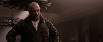 Movie still from “The Book of Eli” (2010), directed by Allen Hughes – A bald man in a brown jacket is looking at the camera; Close Up shot, Over the shoulder angle