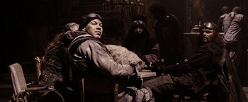 Movie still from “The Book of Eli” (2010), directed by Allen Hughes – A man sitting next to another man with a cat; Medium shot, Low angle