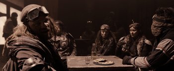 Movie still from “The Book of Eli” (2010), directed by Allen Hughes – A group of people sitting at a table with food; Medium shot, Over the shoulder angle