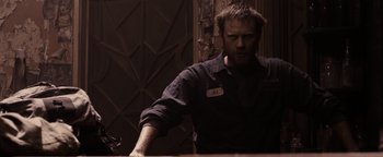 Movie still from “The Book of Eli” (2010), directed by Allen Hughes – A man standing at a counter in front of a door; Medium shot, High angle