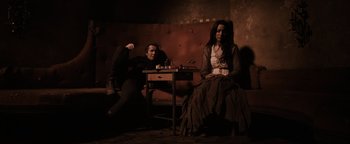 Movie still from “The Book of Eli” (2010), directed by Allen Hughes – A man and a woman sitting at a table in a room; Wide shot, High angle
