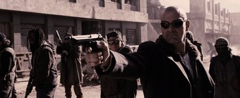 Movie still from “The Book of Eli” (2010), directed by Allen Hughes – A man holding a gun while standing next to another man; Medium shot, Over the shoulder angle