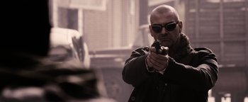 Movie still from “The Book of Eli” (2010), directed by Allen Hughes – A man holding a gun while wearing sunglasses; Medium shot, Over the shoulder angle
