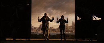 Movie still from “The Book of Eli” (2010), directed by Allen Hughes – A man and a woman standing next to each other in front of a city skyline; Wide shot, Low angle