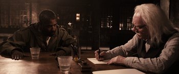 Movie still from “The Book of Eli” (2010), directed by Allen Hughes – Two people sitting at a table writing on paper; Medium shot, High angle