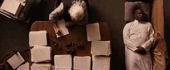 Movie still from “The Book of Eli” (2010), directed by Allen Hughes – An old man writing on a piece of paper on top of a table; Medium shot, Overhead angle