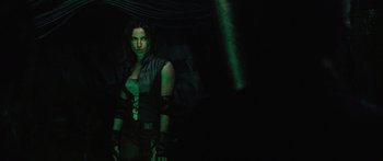 Movie still from “Pandorum” (2009), directed by Christian Alvart – A woman standing in the dark wearing a green outfit; Medium shot, Over the shoulder angle