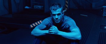 Movie still from “Pandorum” (2009), directed by Christian Alvart – A man sitting on the ground with his arms crossed; Medium shot, Low angle