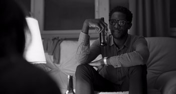 Movie still from “Paris, 13th District” (2021), directed by Jacques Audiard – A man sitting on a couch holding a bottle of beer; Close Up shot, Over the shoulder angle