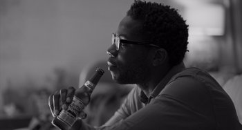 Movie still from “Paris, 13th District” (2021), directed by Jacques Audiard – A black and white photo of a man holding a bottle of beer; Close Up shot, Low angle