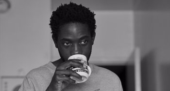 Movie still from “Paris, 13th District” (2021), directed by Jacques Audiard – A man drinking a cup of coffee from a paper cup; Close Up shot, Low angle