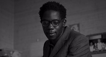 Movie still from “Paris, 13th District” (2021), directed by Jacques Audiard – A black and white photo of a man wearing glasses; Close Up shot, Low angle