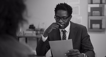 Movie still from “Paris, 13th District” (2021), directed by Jacques Audiard – A man in a suit and tie looking at a piece of paper; Close Up shot, Over the shoulder angle