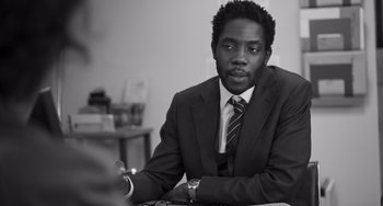 Movie still from “Paris, 13th District” (2021), directed by Jacques Audiard – A man in a suit and tie sitting at a table; Close Up shot, Over the shoulder angle